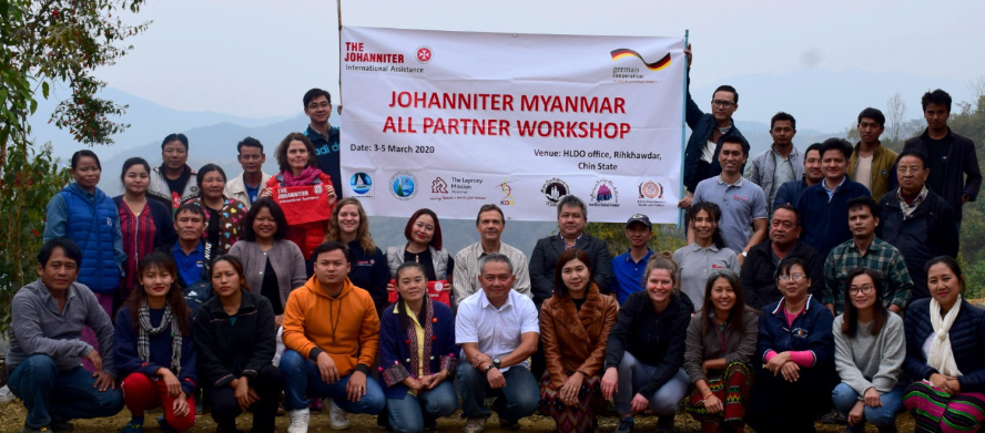 Teilnehmende des Workshophs in Myanmar stehen vor dem Johanniter Logo