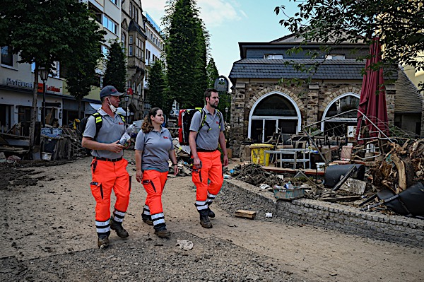 Drei Helfende in Johanniter Uniform in einer von der Flut zerstörten Straße.