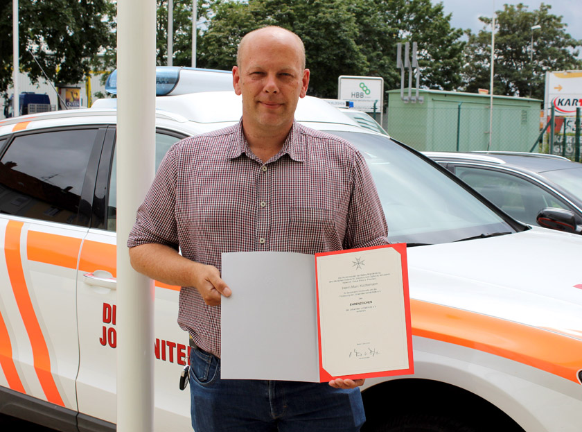 Marc Küchemann steht vor einem Johanniter-Fahrzeug und zeigt sein Ehrenzeichen