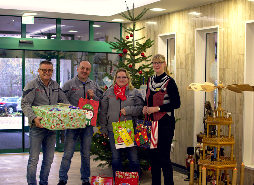 Johanniterinnen und Johanniter mit Geschenken vor dem Wunschbaum (Tannenbaum mit kleinen Anhängern auf dem die Wünsche der Kinder stehen).