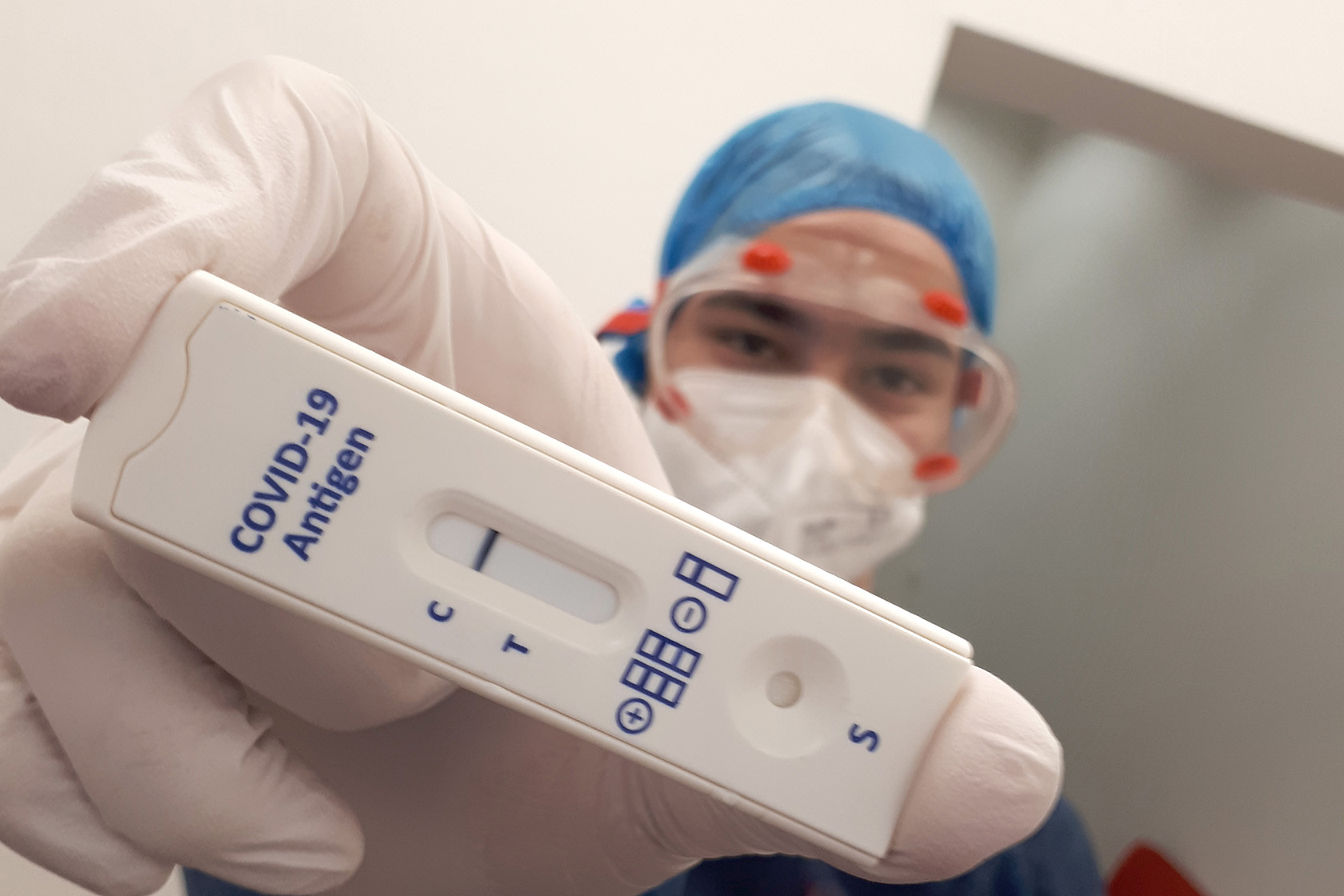 Gegen Corona: Antigen-Schnelltests Ein Mann in Schutzkleidung zeigt einen Corona-Schnelltest
