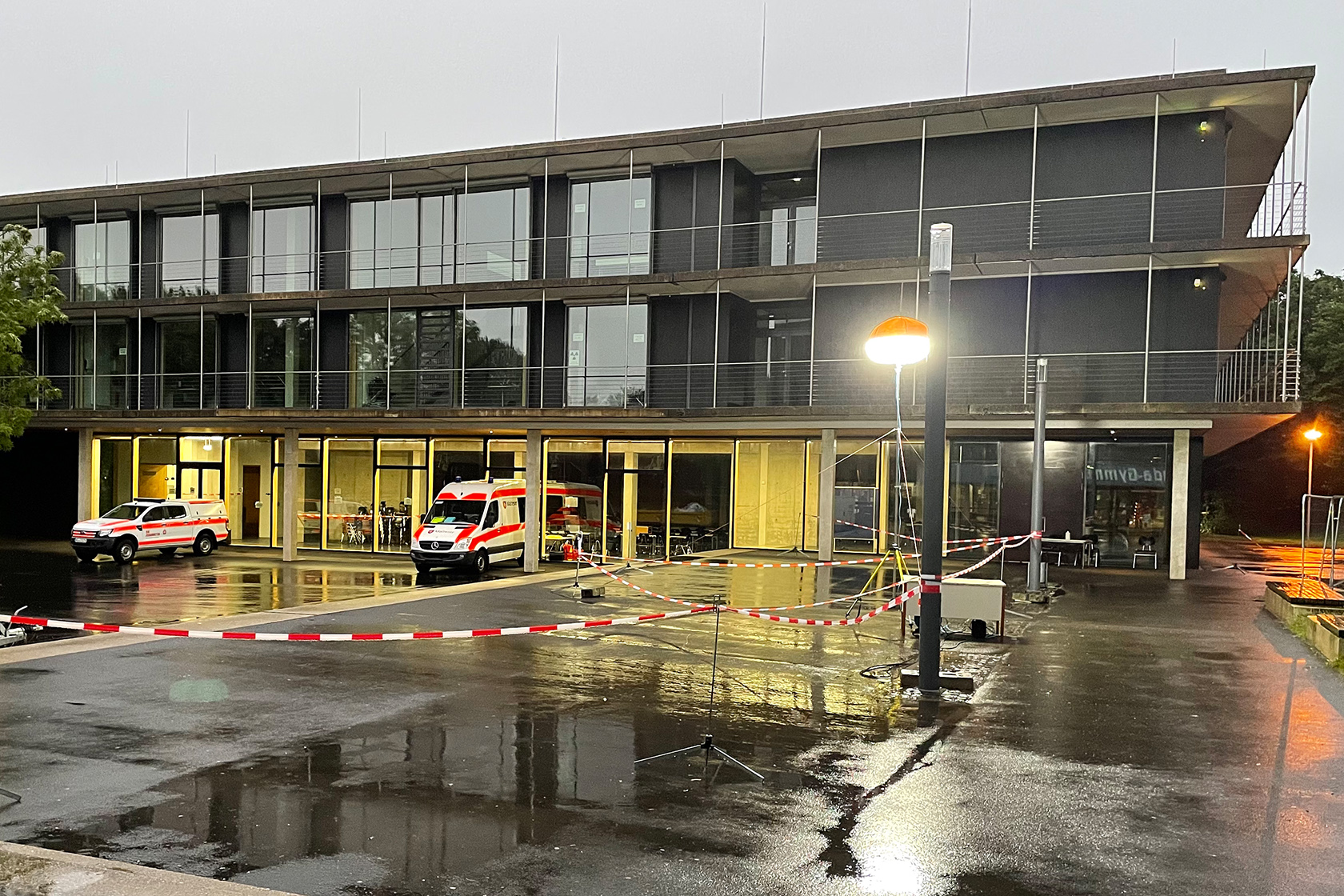 Inda-Gymnasium als Betreuungsstelle Erleuchtetes Schulgebäude mit Fahrzeugen des Bevölkerungsschutz auf dem regennassen Hof.