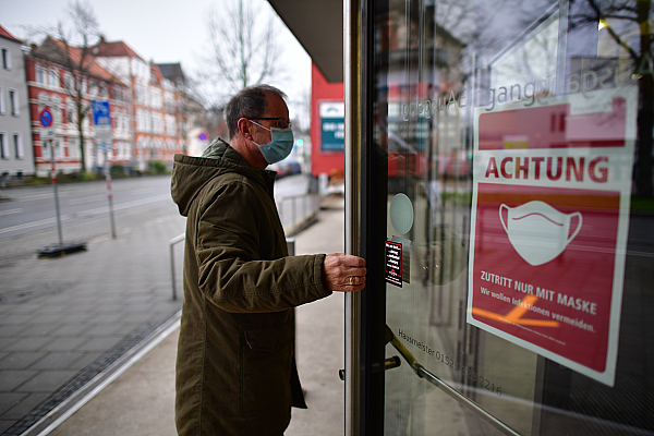 Mann mit Maske öffnet Tür, an der ein Plakat mit der Aufschrift "Zutritt nur mit Maske" klebt.