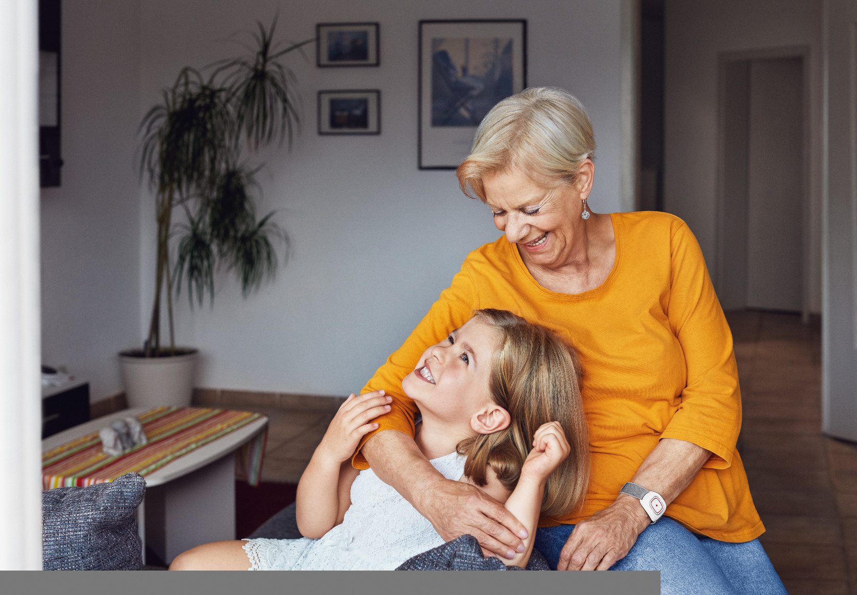 Eine Großmutter mit ihrer Enkelin. Die Oma trägt einen Hausnotruf-Sender am Handgelenk.