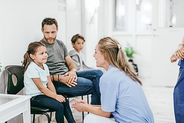 Eine Mitarbeiterin aus dem medizinischen Bereich spricht im Wartezimmer mit einem kleinen Mädchen.