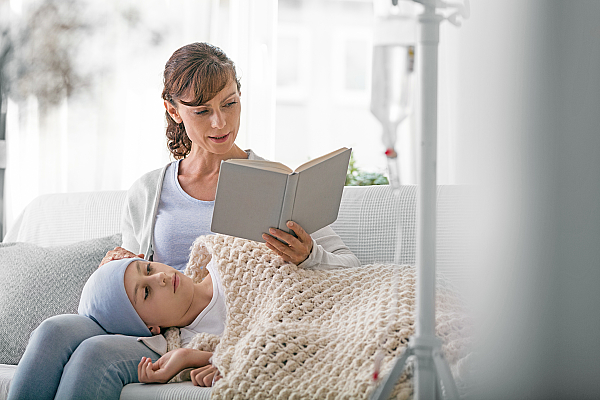 Eine Mutter liest ihrer an Leukämie erkrankten Tochter, die zuhause behandelt wird, aus einem Buch vor.