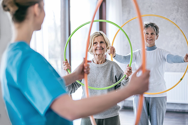 Physiotherapeutin mit zwei Seniorinnen, die Hula Hoop Reifen halten.
