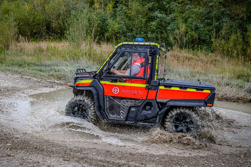 Ein Johanniter-Spezialfahrzeug fährt durch eine große Pfütze auf unwegsamem Gelände.