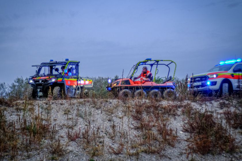 Johanniter-Spezialfahrzeuge und Einsatzwagen mit Blaulicht im Gelände.