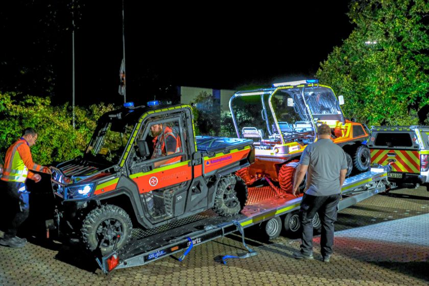 Zwei Johanniter-Geländefahrzeuge, darunter ein ATV, stehen nachts auf einem Anhänger. 