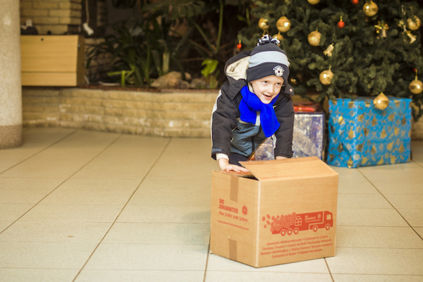 Glücklicher Junge schiebt ein Weihnachtstrucker Paket über den Boden