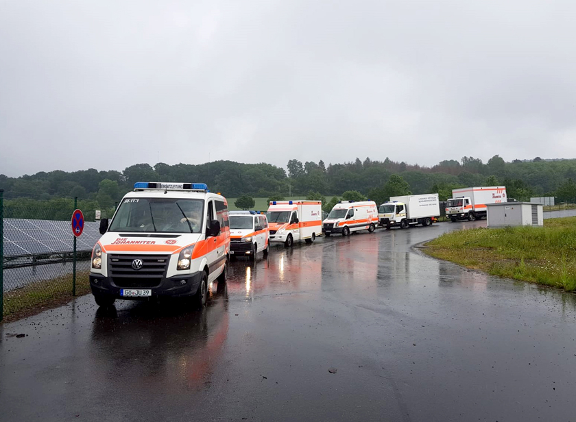 Sechs Johanniter-Fahrzeuge fahren in einer Reihe über eine nasse Straße