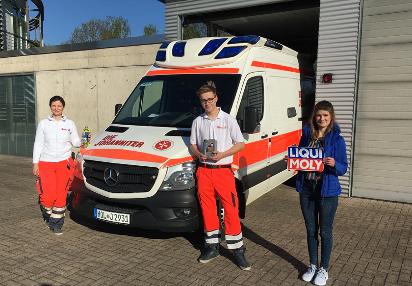 Drei Mitarbeitende der Johanniter aus Holzminden stehen vor einem Einsatzfahrzeug und zeigen Produkte von Liqui Moly.