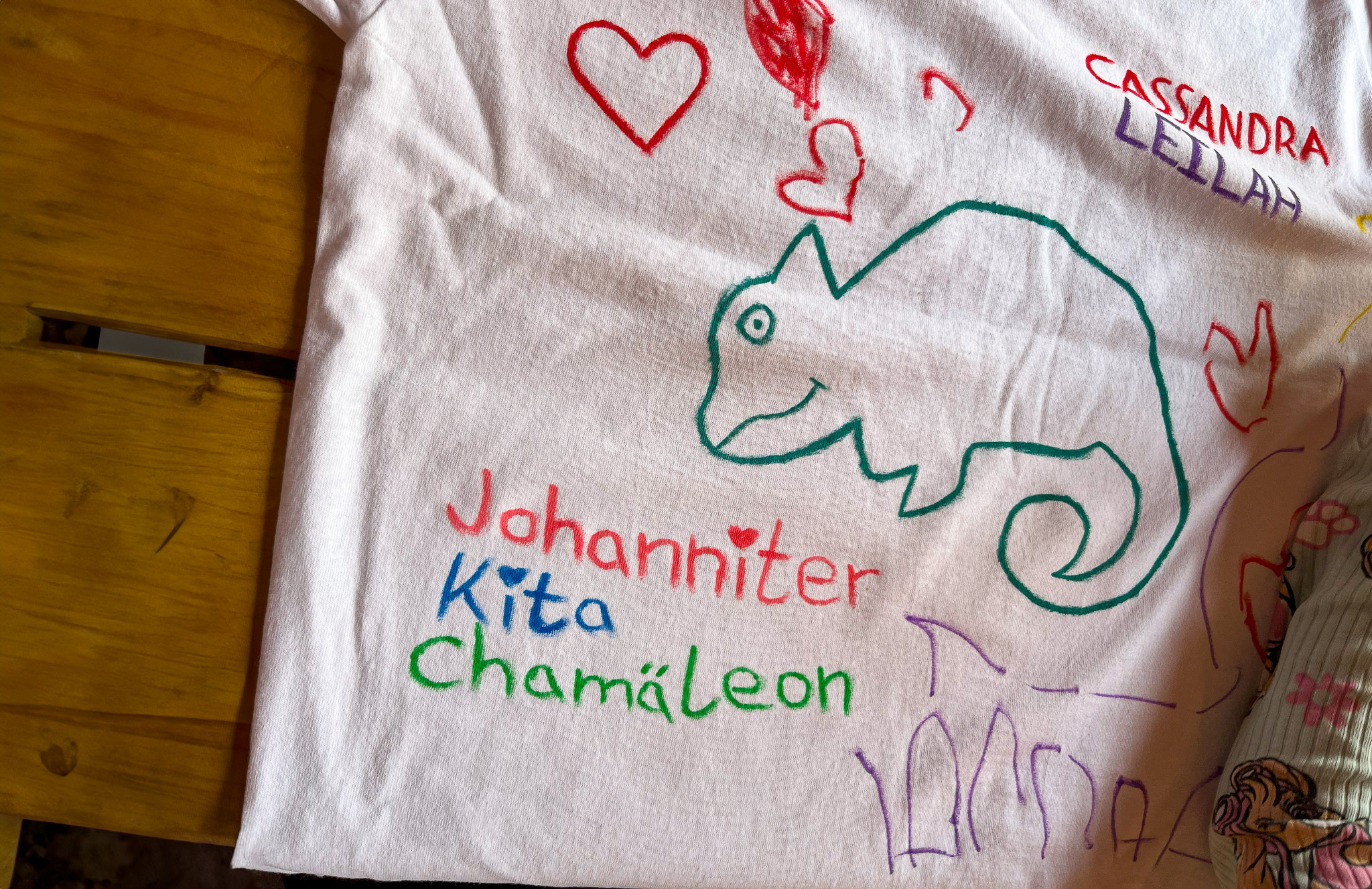 Ein weißes Kinder-T-Shirt bemalt mit einem Chamäleon und beschrieben mit Namen und Johanniter Kita 