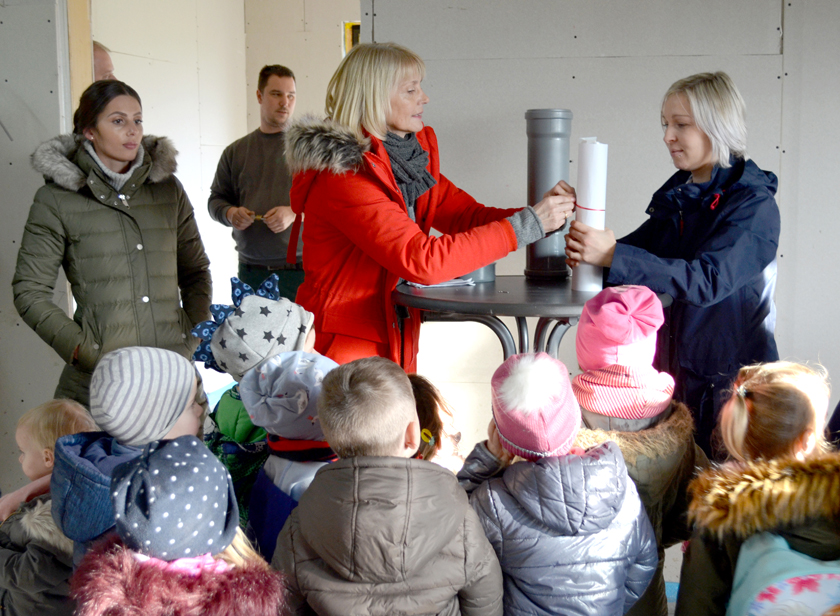 Einrichtungsleitung Nicola Lahl befüllt die Zeitkapsel und die Kita-Kinder schauen ihr dabei zu. 