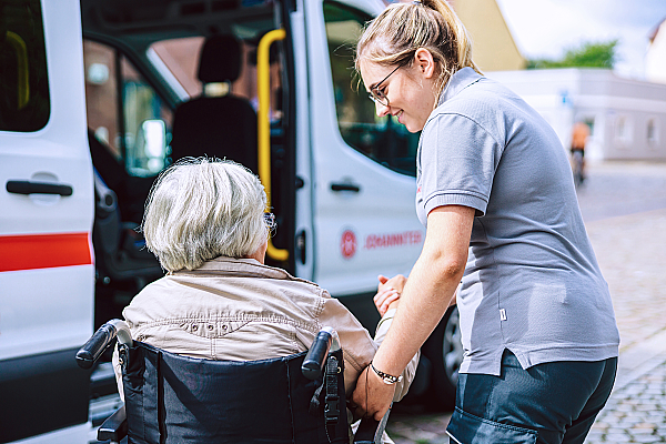 Eine Mitarbeiterin der Johanniter hilft einer älteren Frau im Rollstuhl.