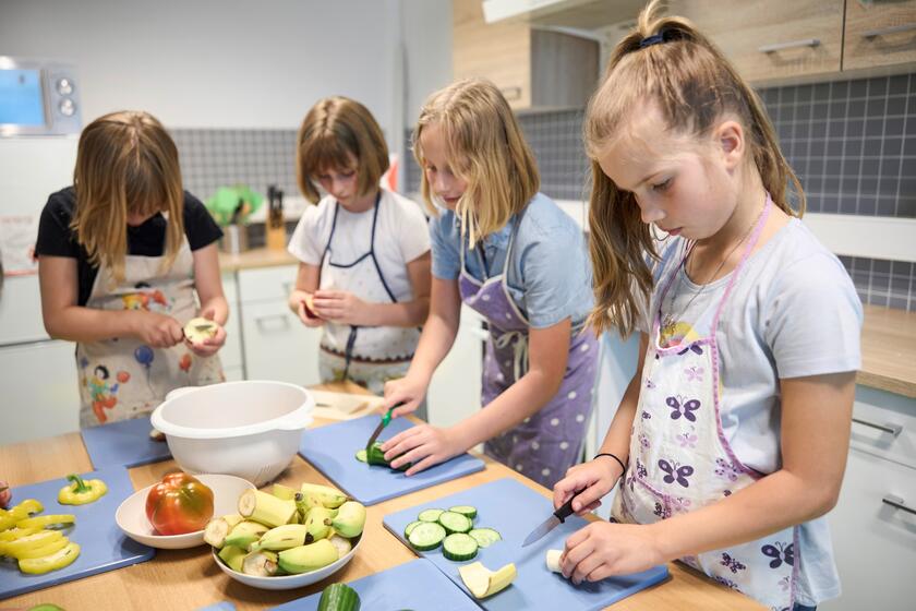 Ganztagsbetreuung im Fliegenden Klassenzimmer Mehrere Schülerinnen schneiden Gurken, Äpfel und Bananen in einer Schulküche.