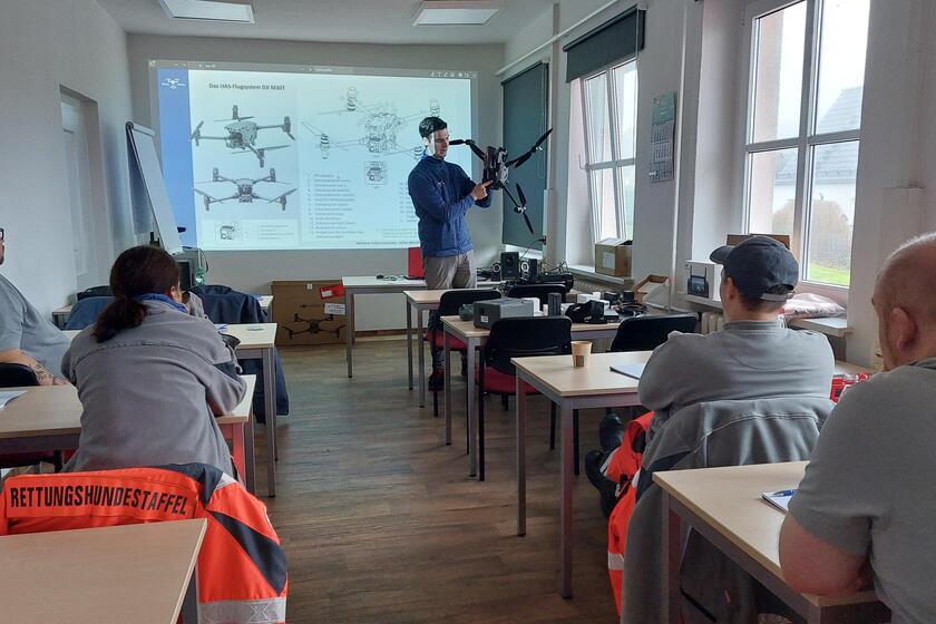 Zu sehen sind vier Personen, die am Unterricht teilnehmen. Vorne steht eine Person, die erklärt, wie eine Drohne funktioniert.
