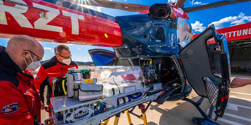 Mannschaft der Johanniter Luftrettung schiebt den Transportinkubator in einen offenen Helikopter