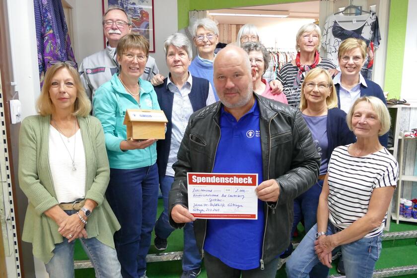 Ein Mann mit einem großen Scheck im Vodergrund umringt von Frauen und einem Mann in Johanniter-Kleidung