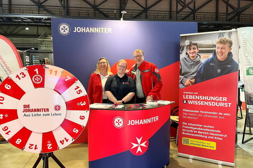 Zwei Johanniterinnen und ein Johanniter an einem Messestand. Links ein Glücksrad.