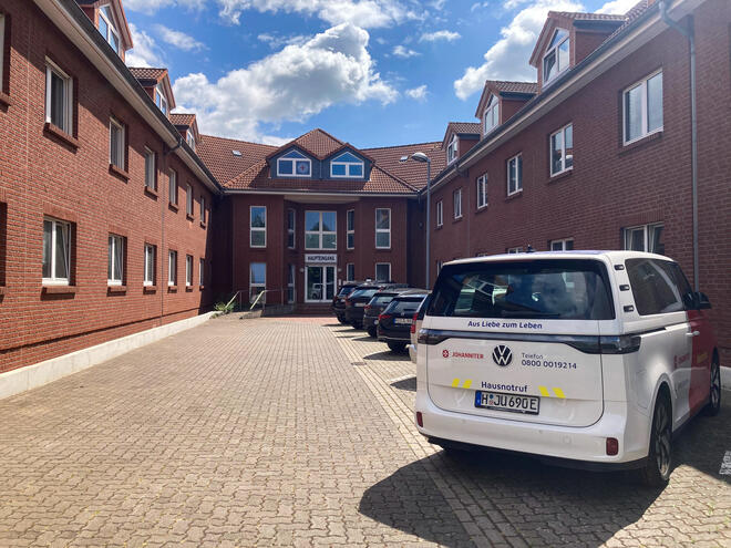 Ein rotes Backsteingebäude mit Innenhof. Ein Johanniter-Fahrzeug steht davor. 