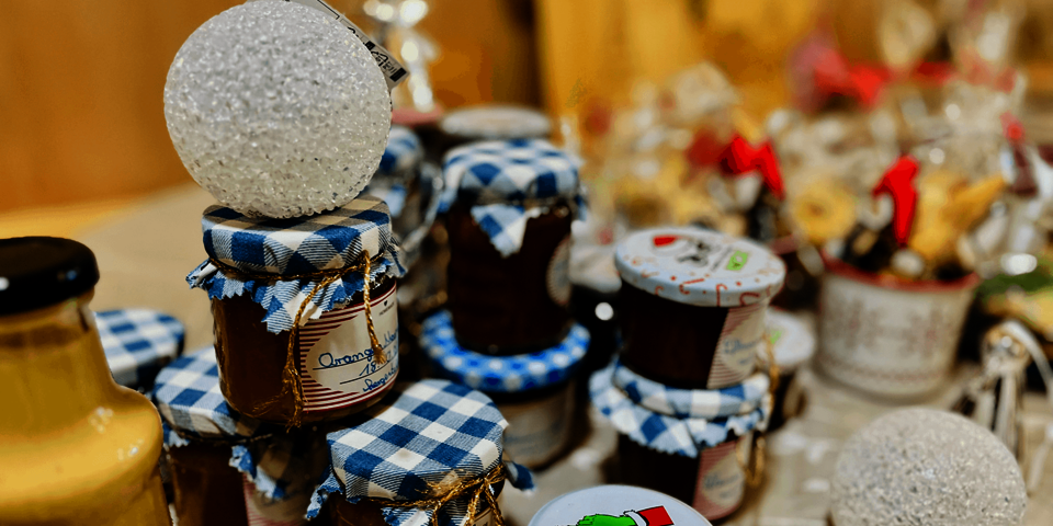 Verschiedene Marmeladengläser mit blau-weiß kariertem Stoffdeckel und handgeschriebenen Etiketten stehen auf einem Tisch, dekoriert mit winterlichen und weihnachtlichen Elementen.