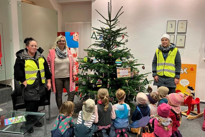 Kinder und drei Frauen bei einem geschmückten Weihnachtsbaum