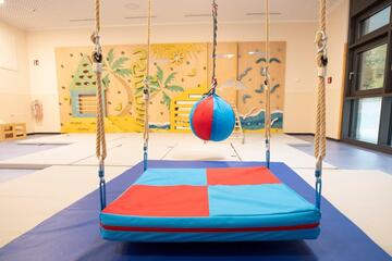 Nahaufnahme der Schaukeln und des freischwebenden Balls im Turnraum mit Kletterwand der Kita Lumi Natura.