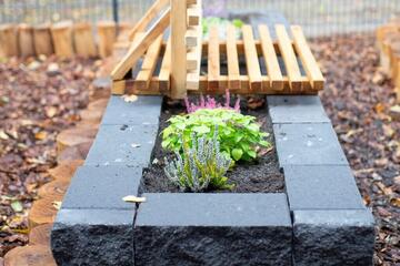 Ein Hochbeet mit Steinumfassung mit einer Bank im Hintergrund.