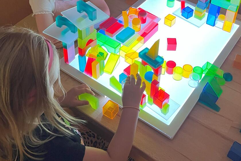 Kind spielt auf einer Leuchtplatte mit bunten Formen.