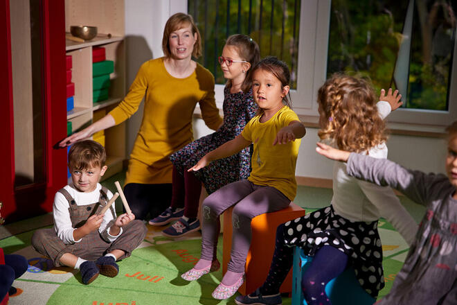 Johanniter Erzieherin macht mit Kindern Bewegungsspiele im Gruppenraum.
