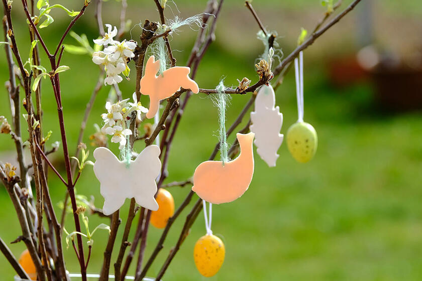 Bunte Anhänger in Schmetterlings- und Hasenform schmücken einen Osterstrauch. 
