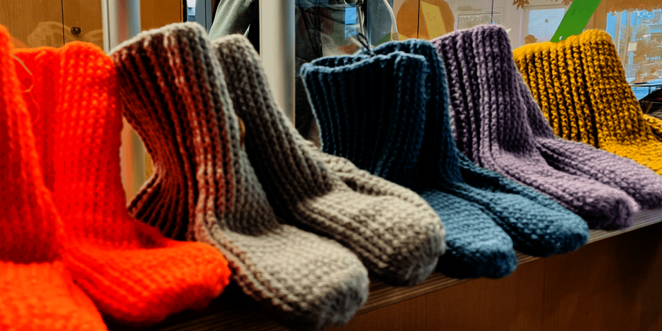 Strickwaren, insbesondere bunte dicke Wollsocken in verschiedenen Farben, sind ordentlich nebeneinander auf einer Fensterbank ausgelegt.