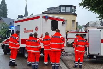 Einsatzkräfte der Johanniter in Stolberg stehen vor einem Gerätewagen der Johanniter.