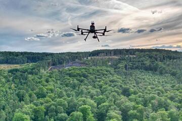 Eine Drohne der Johanniter schwebt über einem Wald, der an manchen Stellen brennt. 
