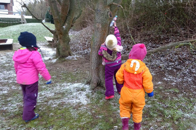 Kita-Kinder verstecken die Flaschenpost an einem Baum.