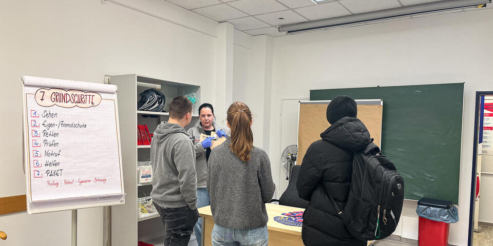 Einige Schüler und Schülerinnen hören einer Frau in Johanniter-Bekleidung zu