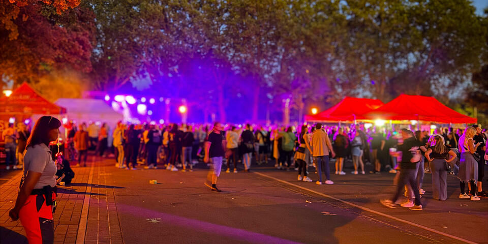 Eine Johanniterin steht an der Seite und schaut auf eine Menschenmenge. Es ist Nacht und im Hintergrund ist eine Bühne mit Lichteffekten