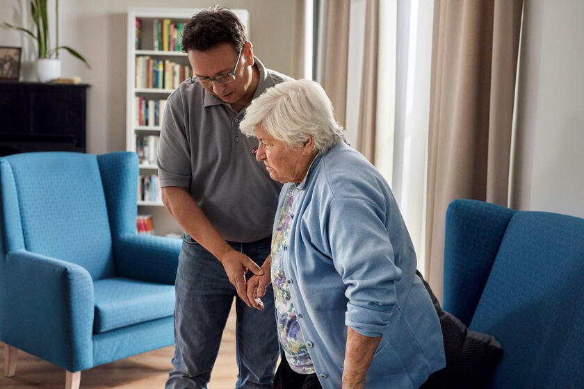 Nachbarschaftshilfekurs Ein Mitarbeiter aus der Pflege hilft einer Seniorin beim Aufstehen.