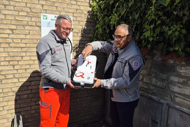 Zwei Männer in Johanniter Kleidung erklären einen Defibrillator 