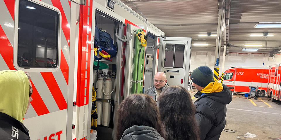 Schülerinnen und Schüle stehen mit einem Mann in Johanniter-Kleidung neben einem Rettungswagen