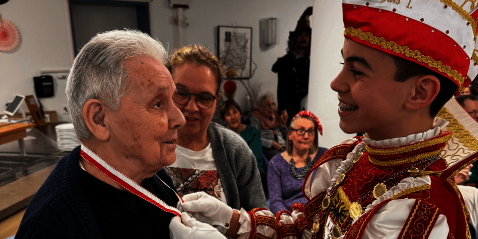Kinderprinz legt einer älteren Person eine Medaille um den Hals.