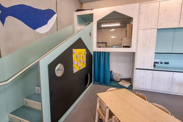 Helle Kita-Ecke mit Sitznische hinter Vorhang und Spielpodest neben Fenstern.