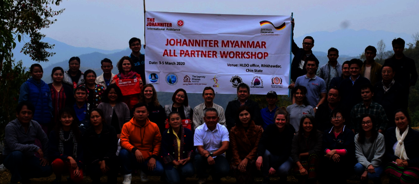 Teilnehmende des Workshophs in Myanmar stehen vor dem Johanniter Logo