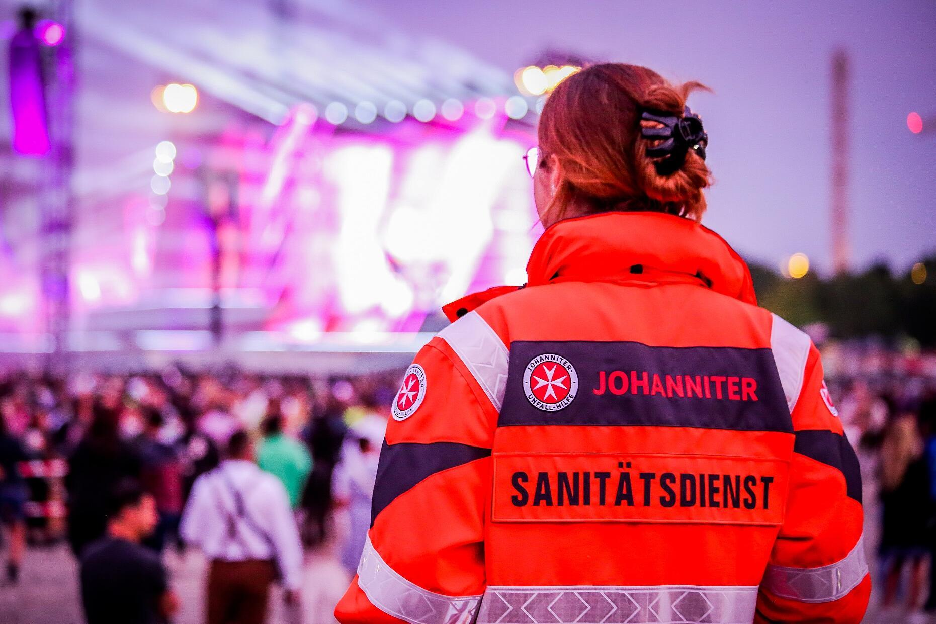 Eine Sanitäterin der Johanniter schaut bei einer Großveranstaltung auf eine Bühne und die davorstehende Menschenmenge.
