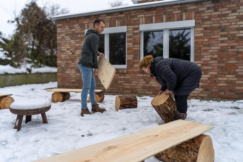 Filip Krubeck (Leiter des Johanniter-Wohnhauses) und Claudia Bettinger (Einrichtungsleiterin Johanniter-Quartier Lübeck) rücken die Holzstämme und Bretter zurecht. Hier können die Kinder und Jugendlichen ab sofort ihren Gruppenrat veranstalten oder am Abend an der Feuerschale zusammensitzen.