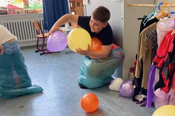 Kinder spielen Sackhüpfen mit Luftballonfangen.