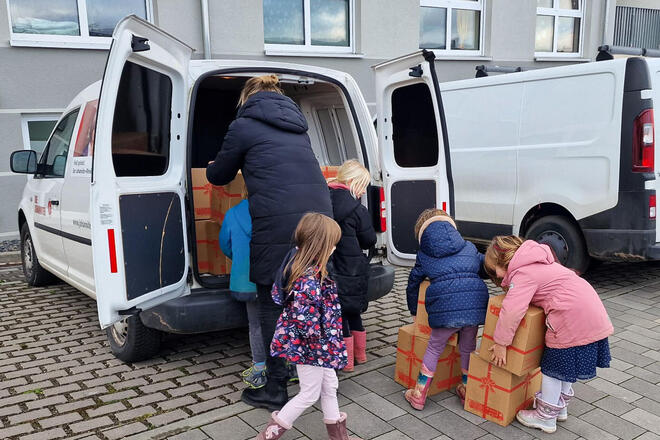 Kinder und eine Frau laden Weihnachtstrucker-Pakete in ein Auto.