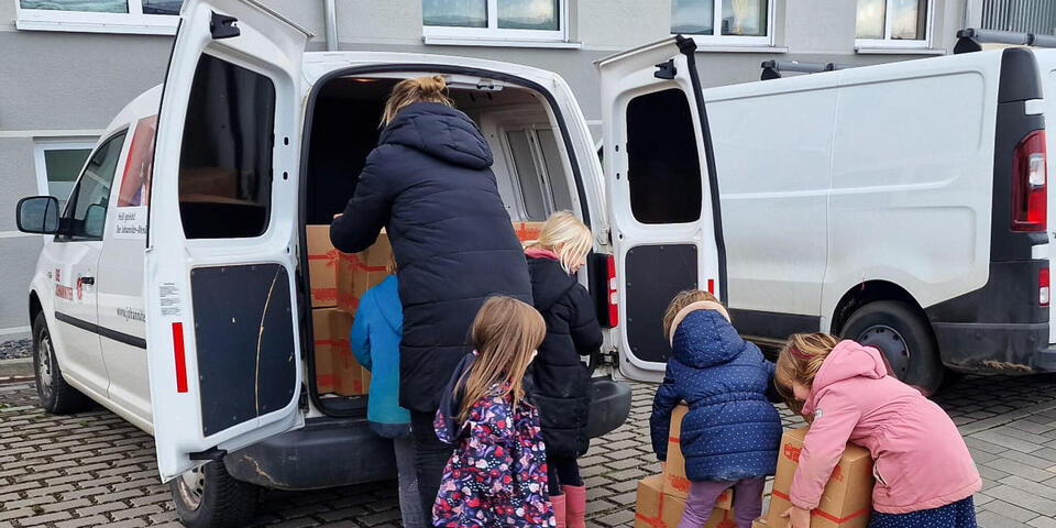 Kinder und eine Frau laden Weihnachtstrucker-Pakete in ein Auto.